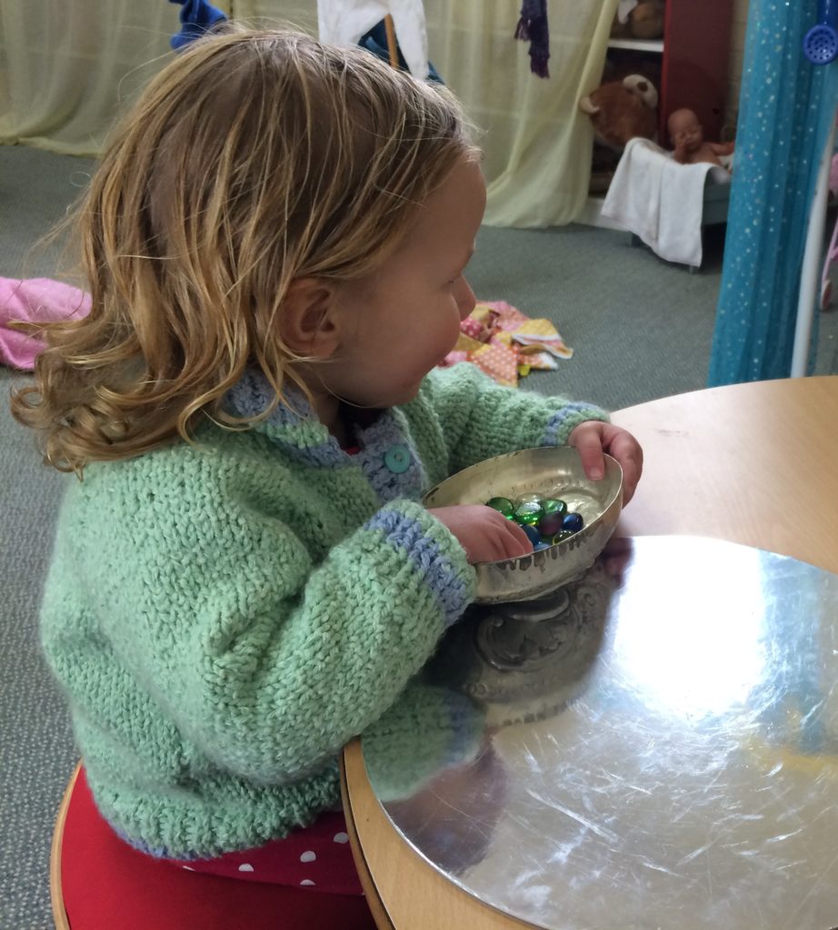 Young child has coloured glass gems and a mirror flat on the table