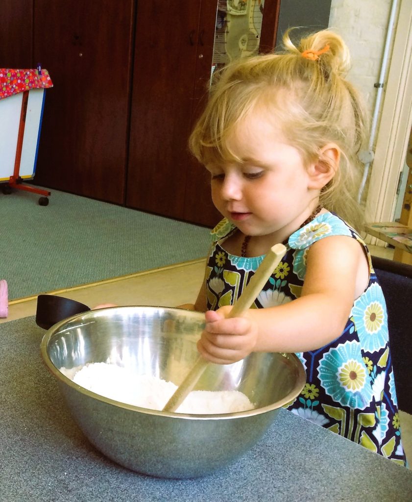 Picture of a toddler stirring a bowl of flower. Cooking helps young children develop math skills